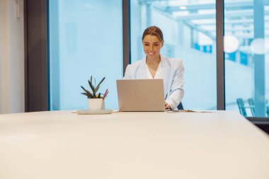 Odaklanmış ve azimli profesyonel bir kadın, parlak, modern ve ilham verici bir ofis ortamında dizüstü bilgisayar kullanıyor.