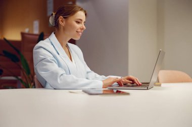 Profesyonel bir kadın, elinde dizüstü bilgisayarla çağdaş bir ofis masasında otururken işine odaklanmış..