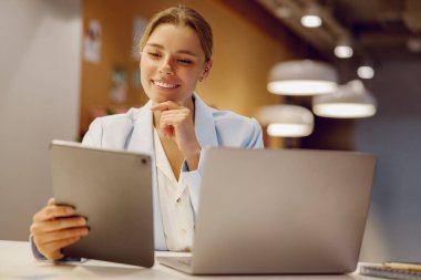 Modern ofis verimliliğini ustalıkla sergileyen, tabletini ve laptopunu aktif olarak kullanan profesyonel bir kadın.