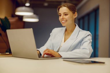 Kendini işine adamış ve işine odaklanmış bir iş kadını dizüstü bilgisayarında parlak ve modern bir ofis alanında daktilo yazıyor.