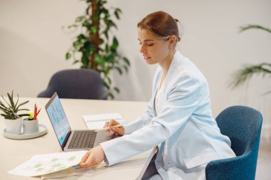 Son derece odaklanmış profesyonel bir kadın, çağdaş ofis ortamındaki çeşitli belgeleri özenle inceliyor.