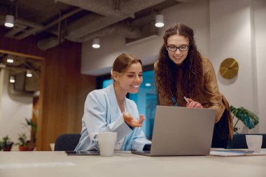 Gösterişli bir ofis ortamında dizüstü bilgisayarla iş birliği yaparken proje detaylarını tartışan iki profesyonel.