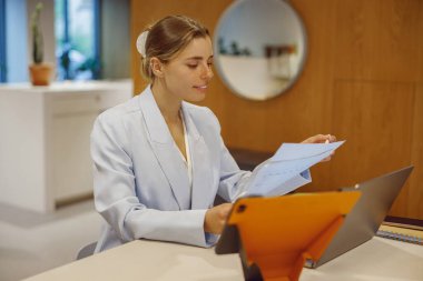 Şık, modern ofis masasında çeşitli kağıtları derinden analiz eden kararlı ve odaklanmış bir iş kadını.