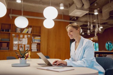 Kendini işine adamış ve işine odaklanmış bir kadın laptopunu üretkenlik için tasarlanmış şık ve modern bir ofis ortamında kullanıyor.