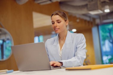 Kendini işine adamış ve işine odaklanmış profesyonel bir kadın laptopuyla düzenli ve modern bir çalışma alanında meşgul oluyor.