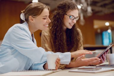 Sıcak bir kahve dükkanında, iki kadın bir tablet kullanarak bir projede işbirliği yapıyor ve beyin fırtınası yapıyorlar.