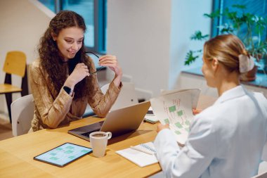 İki profesyonel, parlak bir ofis ortamında dijital cihazları kullanarak derin bir tartışmaya giriştiler.