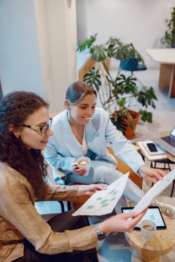 İki kadın modern bir ofis ortamında etkin bir şekilde işbirliği yaparken çeşitli belgeleri tartışıyorlar.