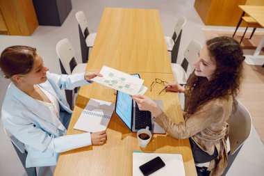 İki kadın yenilikçi fikirleri tartışırken şık bir çalışma masasında önemli belgeleri paylaşıyorlar.
