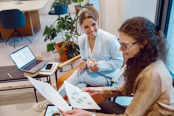 İki kadın, şık bir ofis alanında dijital araçlar kullanarak yenilikçi fikirler hakkında tartışıyorlar.