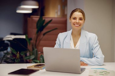 Dizüstü bilgisayarında kendine güvenen bir iş kadını, profesyonelliği ve yeniliği yansıtan şık bir ofiste çalışmaya hazır.