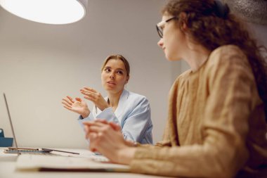 Modern bir ofiste iki kadın yenilikçi fikirleri paylaşıyor, düşünceli bir tartışma ve işbirliği sergiliyorlar.