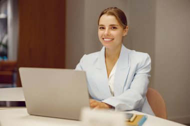 Gülümseyen iş kadını dizüstü bilgisayarıyla meşgul, çağdaş bir çalışma alanında profesyonelliği temsil ediyor..