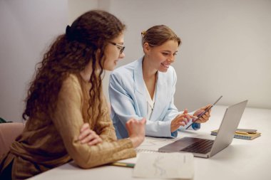 İki kadın, çağdaş bir çalışma ortamında dizüstü bilgisayar kullanırken yapıcı bir tartışmaya tutuştular.