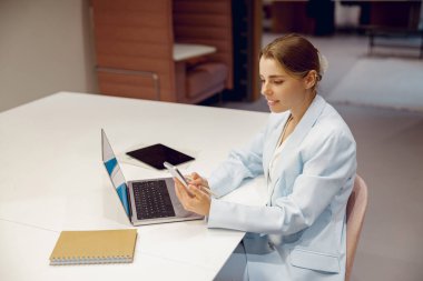 Kendini işine adamış bir profesyonel, dizüstü bilgisayarını ve telefonunu modern bir çalışma alanında etkin bir şekilde kullanır.