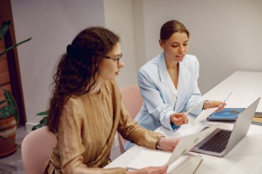 Modern ofis ortamında fikirleri tartışan iki profesyonel, işbirliği ve stratejiye odaklanıyor.