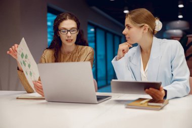 İki iş kadını modern bir ofiste yenilikçi fikirleri tartışırken bir dizüstü bilgisayardaki bilgileri gözden geçiriyorlar.