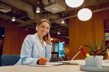 Gülümseyen ve profesyonel bir kadın modern dekor unsurlarının yer aldığı şık bir ofis masasında kendini işine vermiş.