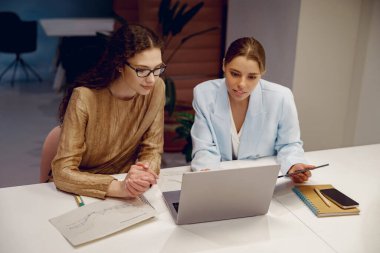 Modern bir ofiste, iki profesyonel çözüm üretmek için dizüstü bilgisayarda çalışırken fikirleri tartışırlar.