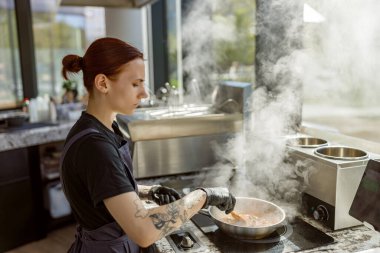 Yetenekli bir şef, buharla dolu modern bir mutfakta ustaca lezzetli bir yemek hazırlar.