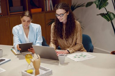 İki profesyonel, şık bir ofis ortamında dizüstü bilgisayar ve tabletlerle verimli bir toplantı yapıyorlar..