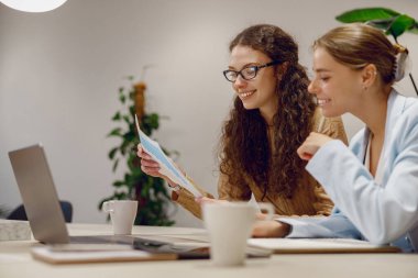 Modern bir çalışma alanında, iki kadın aktif olarak bir dizüstü bilgisayarla iş birliği yapıyor, etkin bir takım çalışması örneği oluşturuyor.