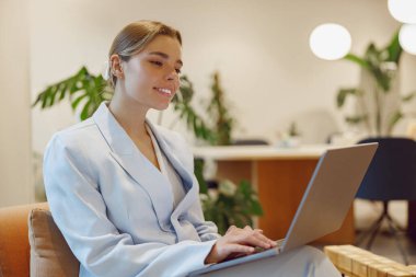 Şık bir takım elbise giymiş odaklanmış bir kadın şık bir ofis ortamında dizüstü bilgisayarıyla çok meşgul.