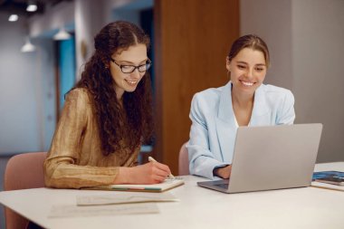 İki yetenekli profesyonel, bir dizüstü bilgisayar ve notlarına odaklanarak, gösterişli bir çalışma alanında iş birliği yapıyorlar.