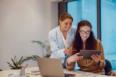 Modern bir ofiste, iki kadın etkili bir takım çalışması ve teknoloji sunan bir tabletle işbirliği yapıyor.