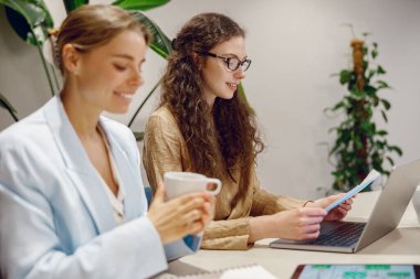 İki kadın, modern ofis ortamında aktif olarak iş birliği yapıyor. İşlerine odaklanmış ve tamamen meşgul.