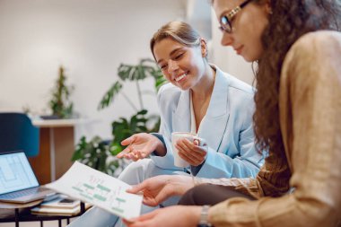 İki profesyonel kadın, modern bir ofiste işbirliği ve takım çalışmasını ön plana çıkaran yenilikçi bir projeyi tartışıyor