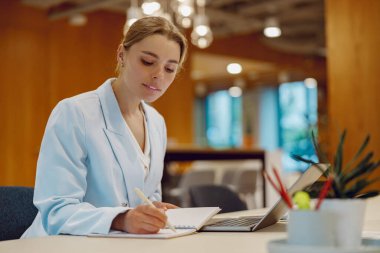 Şık ve şık bir ofis ortamında kendini adamış bir sağlık uzmanı özenle notlar yazar.
