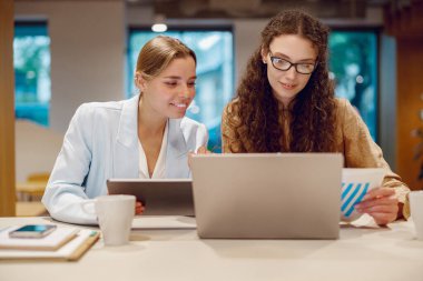 İki profesyonel, iyi aydınlatılmış ve parlak bir ofis ortamı içinde bir dizüstü bilgisayar üzerinde etkili bir şekilde işbirliği yapıyorlar.