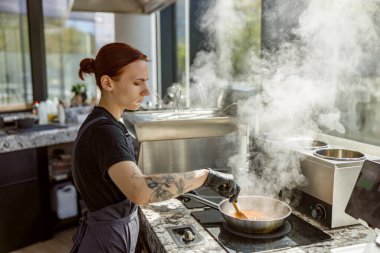 Odaklanmış bir şef modern bir mutfakta lezzetli bir yemek hazırlar, tencereden buhar yükselir.