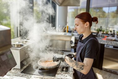 Yetenekli bir aşçı şık bir mutfakta yemek hazırlıyor. Buhar güzelce yükseliyor.
