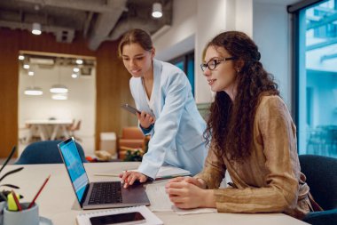 İki yetenekli profesyonel aktif olarak iş birliği yapar ve şık bir ofis içinde bir dizüstü bilgisayarda fikirleri paylaşırlar.