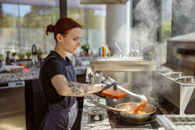 Çok yetenekli bir aşçı modern bir mutfakta lezzetli ve aromatik soslarla dolu bir tencereyi incelikle karıştırır.