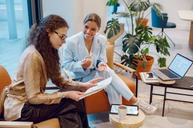 Modern bir ofis ortamında, iki kadın birlikte üretken ve işbirlikçi bir tartışmaya girerler.