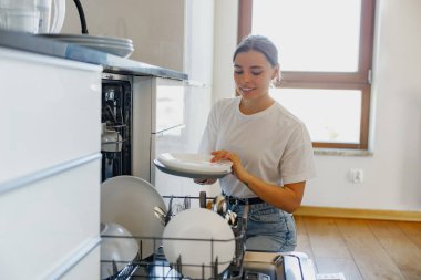 Bir kadın, pırıl pırıl temiz tabaklarını güzel stil bir mutfakta düzenler ve ev hayatını gözler önüne serer.