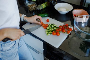 Bir insan şık bir mutfakta ustalıkla taze domates ve canlı salatalıklar doğruyor. Yemek hazırlama sanatını ön plana çıkarıyor.