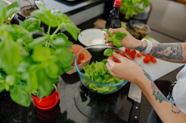 Güzel, modern bir mutfak ortamında taze fesleğen ve olgun domates kullanarak canlı bir salata hazırlıyorum.