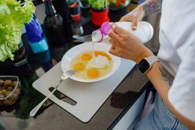 Modern bir mutfak ortamında yumurtaları ustalıkla hazırlayan bir insan taze ve canlı malzemelerden oluşan bir seçim sergiliyor.