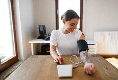 Bir kadın dijital tansiyon monitörü kullanıyor. Parlak ve davetkar ortamında. Sağlık için.