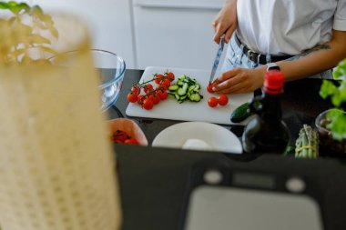 İyi aydınlatılmış, çağdaş bir mutfak alanında bir dizi taze sebzeyi ustalıkla doğrayan bir birey.