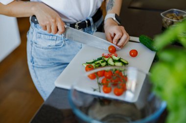 Canlı domatesleri ve taze salatalıkları kesme tahtasına koyup sağlıklı yemekler hazırlayan biri.