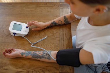 Dijital tansiyon monitörü kullanan bir kişi, sağlık bilincini ve etkili ev bakımını vurguluyor