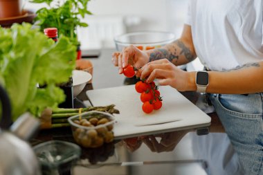 Bir insan titizlikle taze ve olgun domatesleri canlı sebzelerle dolu şık bir mutfakta hazırlıyor.
