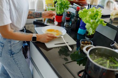 Bir insan, taze otlar ve çeşitli malzemelerle dolu şık bir mutfakta lezzetli bir yemek pişirmekten mutluluk duyar.