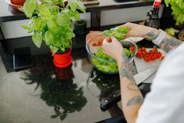 Yetenekli bir insan, modern bir mutfakta taze yeşillik ve kiraz domatesli sağlıklı bir salata yapıyor.