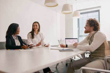 İyi aydınlatılmış bir ofis ortamında, üç yetenekli profesyonel canlı bir işbirliği toplantısına katılıyor.